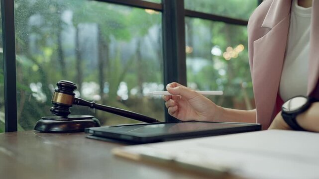 Female hand using stylus to write or sign digital legal document, gavel beside symbolizes law and order