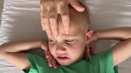 Closeup of child face during osteopathy session with doctor hands on forehead, brow points and crown. Boy shows capricious reaction, reaching hands to neck and starting to cry during treatment.