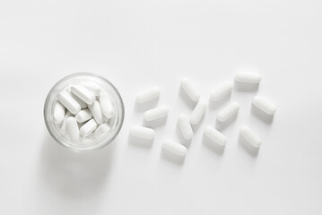 Large long oblong white pills in glass bowl on white background	