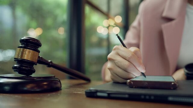 Female legal professional writing documents digitally on tablet, gavel symbolizing law and order