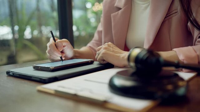 Modern female lawyer writing legal notes on tablet, gavel beside her symbolizes justice and authority