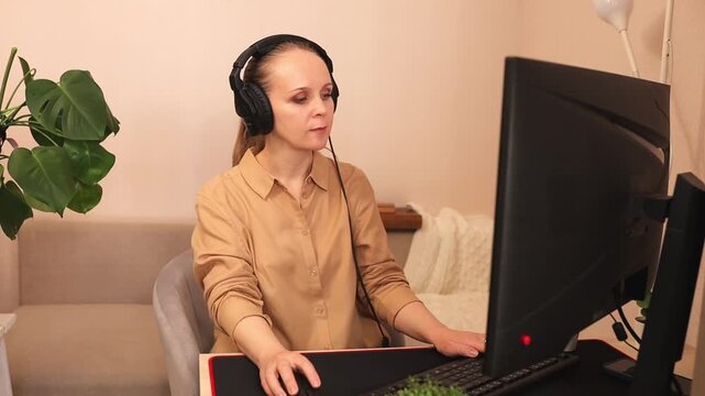 A focused young white woman is working on a computer at her desk. She's wearing headphones. Listening to music.