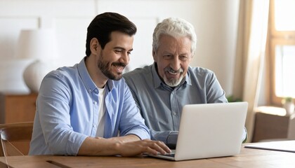 Obraz premium Elderly father and son sitting at a desk, looking at a laptop. Two generations using technology together