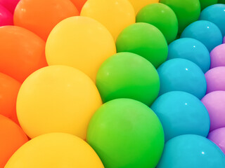 Background of colorful balloons with rainbow pattern, up close. Backdrop of bright color arrangement of latex balloons for decoration. Classic balloon type made from natural, biodegradable materials.