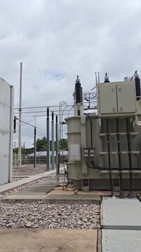 Cinematic pan of high voltage electrical substation switchyard with power transformers and porcelain insulators against cloudy sky for energy industry.
