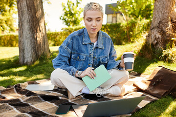 Young woman enjoys a sunny walk in nature while sipping coffee and working on her laptop