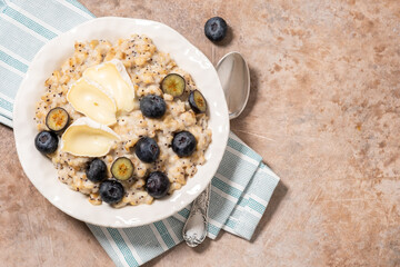 A bowl of oatmeal with blueberries, camembert cheese and poppy seeds