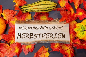Holzschild mit der Aufschrift WIR WÜSCHEN SCHÖNE HERBSTFERIEN und herbstliche Dekoration