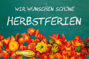 Schultafel mit der Aufschrift WIR WÜSCHEN SCHÖNE HERBSTFERIEN und herbstliche Dekoration