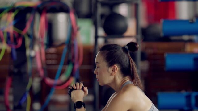 Fit Asian woman training hard in gym wearing gloves, sweating from intense exercise. Displays strength, resilience and health focus.
