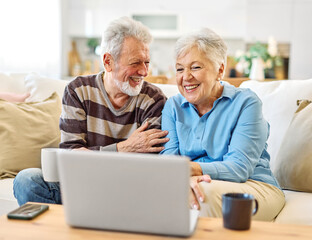 Portrait of a lovely senior mature couple using a laptop together and having video call sitting on sofa at home