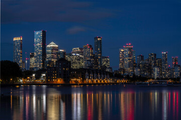 Obraz premium The city skyline of Canary Wharf and the Isle of Dogs seen at night with reflections of the lights in the water. Landscape or horizontal orientation.