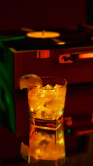 Golden cocktail with lime slice in glass beside vintage vinyl record player in neon ambiance. Concept of bar culture, luxury lifestyle, creative marketing, and emotional nightlife experiences.
