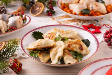 Classic Christmas food medley on a decorated table. Fish, dumplings stuffed with cabbage and mushrooms, cheesecake, and ham.