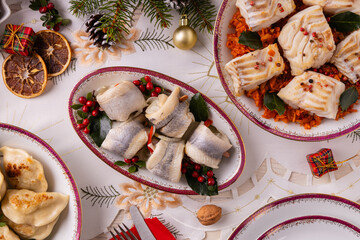Classic Christmas food medley on a decorated table. Fish, dumplings stuffed with cabbage and mushrooms, cheesecake, and ham.