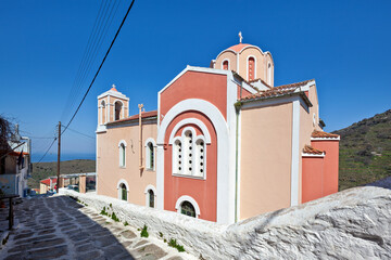 Traditional Greek Orthodox church of Metamorfosi (Transfiguration) with red and white facade in Ioulida, Kea island, Cyclades, Greece, a scenic village architecture under clear blue Mediterranean sky.