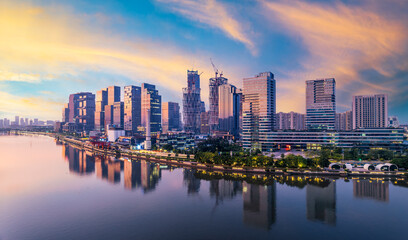 Modern financial district skyline with skyscrapers under construction reflected in the river at sunrise in Guangzhou.