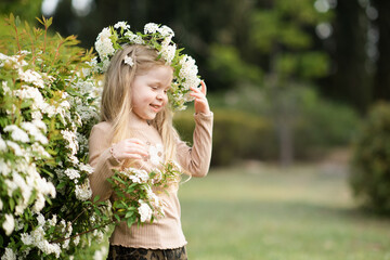 Obraz premium Cute baby girl 3-4 year old wearing floral wreath posing in garden with flowers outdoors. Springtime