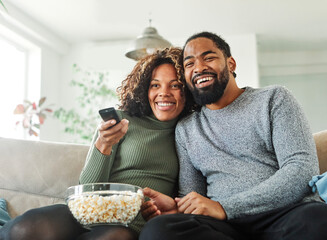 Portrait of a happy young couple watching tv together at home. Shot of a couple resting on the couch watching television