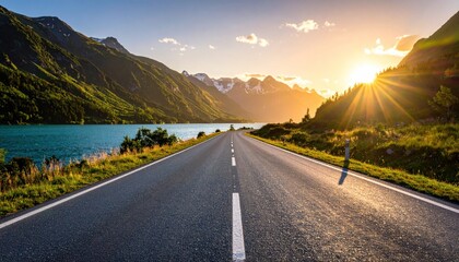Scenic view of a long road leading towards mountains and a lake under a bright, sunny sky.