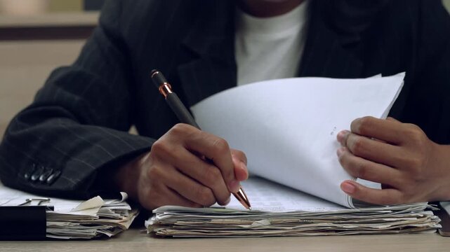 Macro view of hands flipping pages and writing on a large pile of documents, showcasing business and administrative tasks.