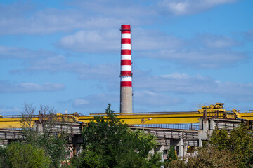 Weathered industrial building with striped smokestack and rooftop machinery under a clear sky.