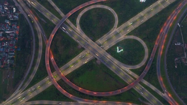 An overhead hyperlapse drone shot of a complex highway interchange in Hanoi, Vietnam, with a cloverleaf design and light traffic.