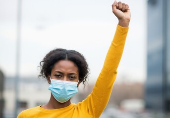 Black woman wearing a face mask raises her fist in protest. Young African American activist at a demonstration. Social justice and empowerment concept
