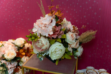 Beautiful floral arrangement showcasing soft pink and white blooms, along with greenery and natural accents, set against a vibrant pink backdrop in a decorated space.