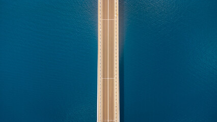 Top-down view of a bridge over the blue sea. Abstract aerial view of the structure used for transportation and commerce. Krk Bridge in Croatia