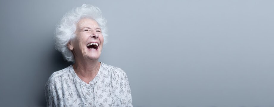 The elderly woman laughing joyfully against a minimalist gray studio background with copyspace