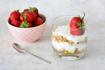 a strawberry parfait decorated with fresh berries in drinking glass with a bowl of strawberries