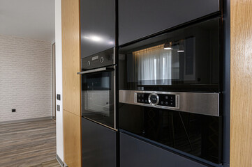 Modern kitchen detail with built-in black ovens and wooden cabinets. Sleek design