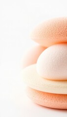 Stacked cosmetic sponges in soft pastel shades against a bright white surface, creating a clean and minimalist aesthetic