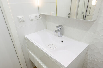 pristine white bathroom sink with a modern chrome faucet. The walls are tiled in a white, textured pattern. A mirror reflects part of a shower
