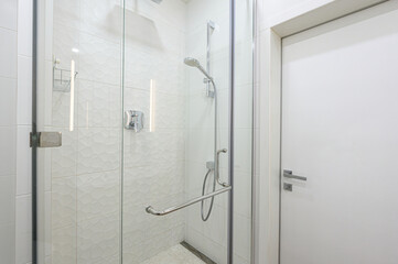 A modern bathroom features a glass-enclosed shower with white textured tiles. Chrome fixtures and a white door provide a clean, minimalist aesthetic