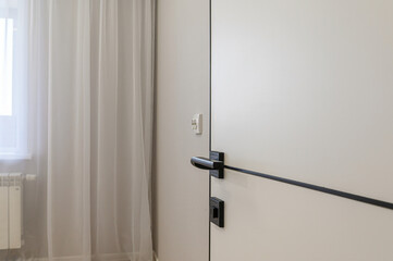 A clean, minimalist interior view featuring a white door with sleek black hardware, complemented by sheer white curtains and a subtle wall color