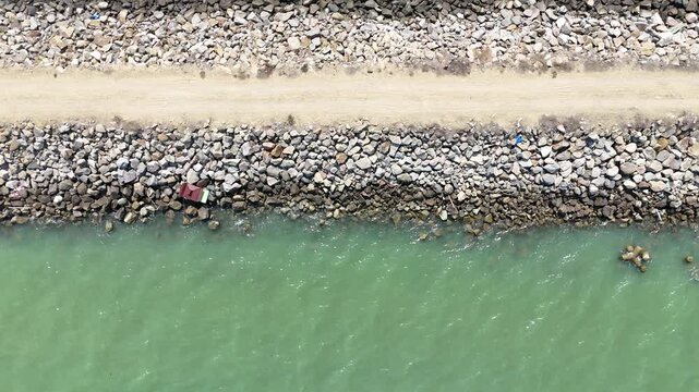 Aerial View of Ocean Meets Stone Barrier and Sandy Path