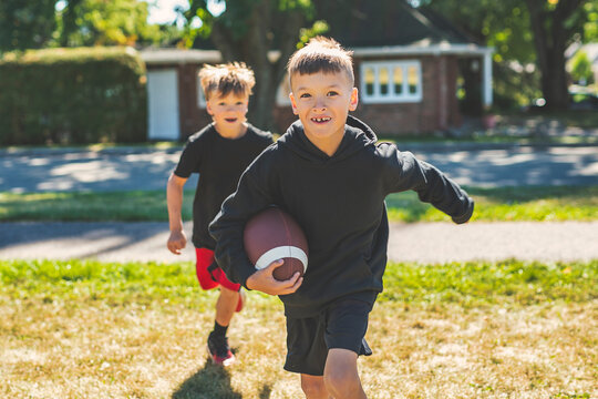 brother playing American football. Kids play football in sunny summer park. - Powered by Adobe