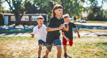 brother playing American football. Kids play football in sunny summer park.