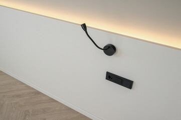 A modern wall with a black lamp and power outlet. The wall is white, and the floor has a parquet...