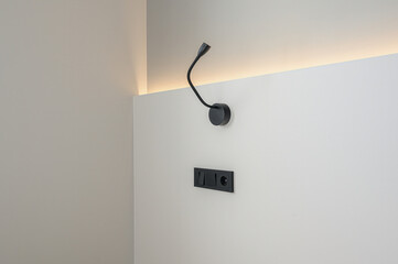 Clean shot of a white wall with a black flexible lamp and electrical outlets. Minimalist, modern...
