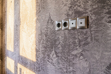 Wall with tree pattern wallpaper, sunlit, with a strip of sockets and a data port