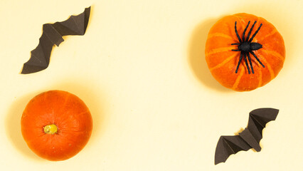 Halloween holiday concept. Frame from orange pumpkins, black bats and spider. Greeting card. Light yellow background.
