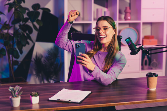 Young woman in a modern home office using her smartphone and microphone setup for streaming content creation - Powered by Adobe