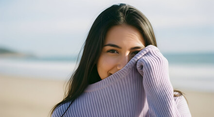 Smiling woman hiding face with lilac sweater at the beach happy carefree young adult female model posing outdoors coastal scene natural light