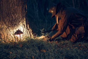 Mysterious plague doctor kneels near tree, illuminated by lantern in dark forest.