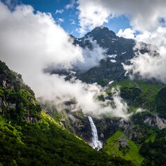 Lush green mountain valley with a cascading waterfall partially obscured by clouds