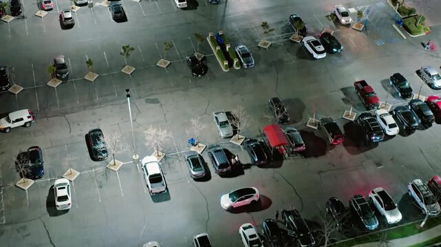 Aerial view captures a parking lot filled with cars at night under streetlights