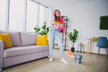 Young woman in a bright cozy apartment smiling while cleaning with a mop, enjoying indoor leisure...